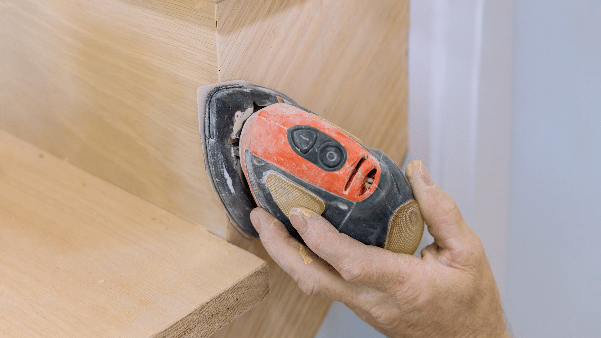 Hands guiding an orbital sander across the wooden tread of a staircase