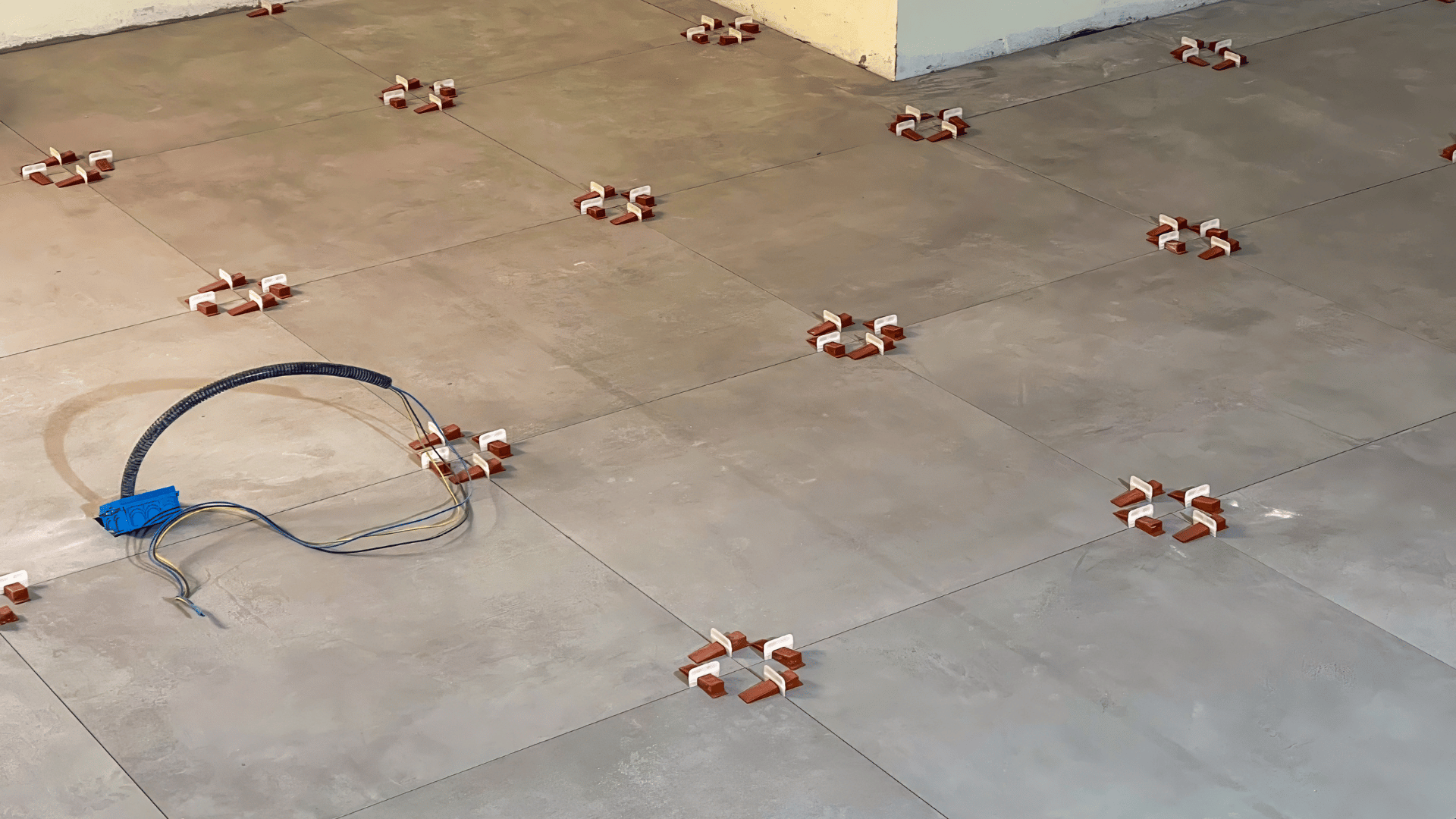 Large-format grey floor tiles freshly laid with red and white leveling clips at each joint