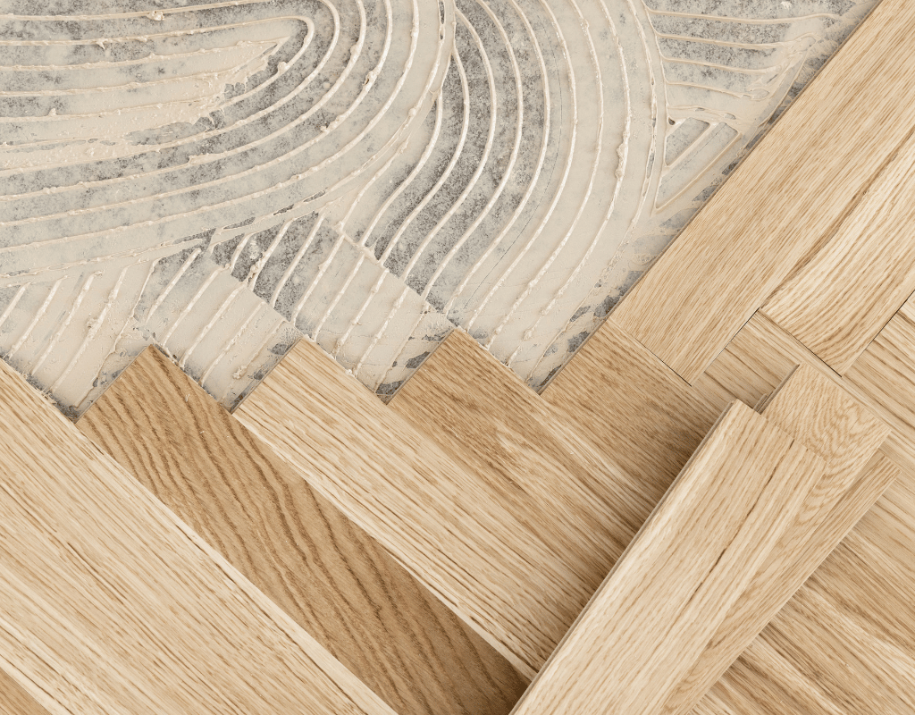 Close-up of a herringbone hardwood floor mid-sanding, with swirl marks separating sanded and unsanded boards
