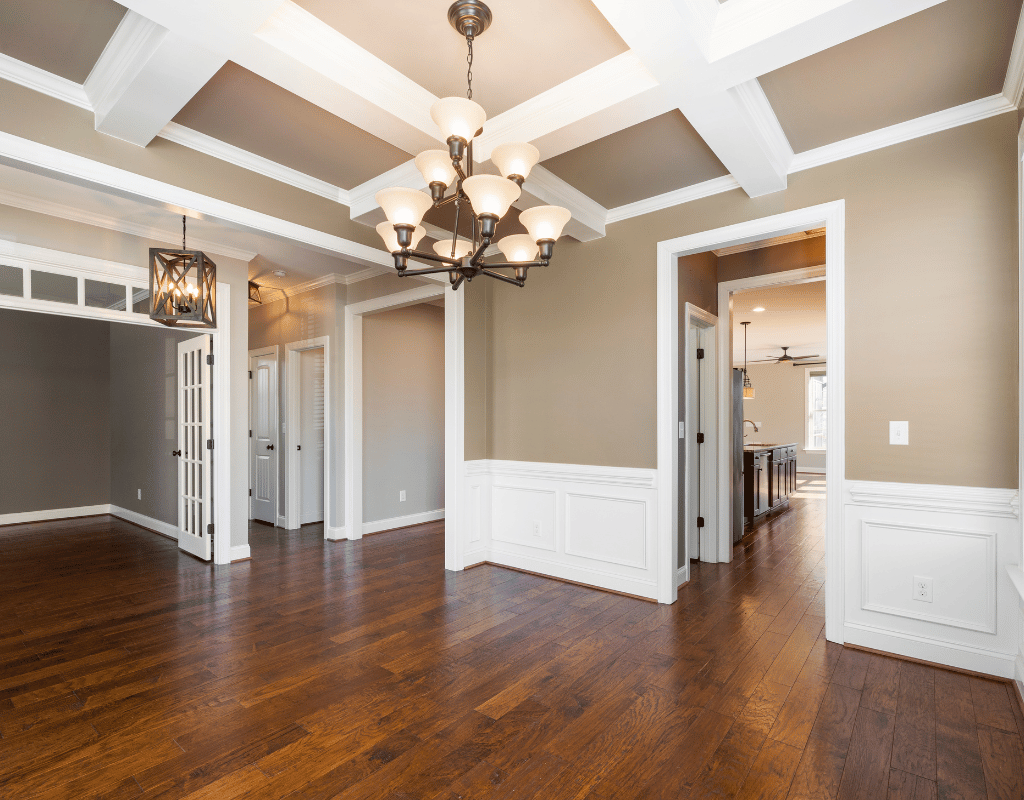 Empty dining room with dark hardwood flooring, white wainscoting, a coffered ceiling and a chandelier
