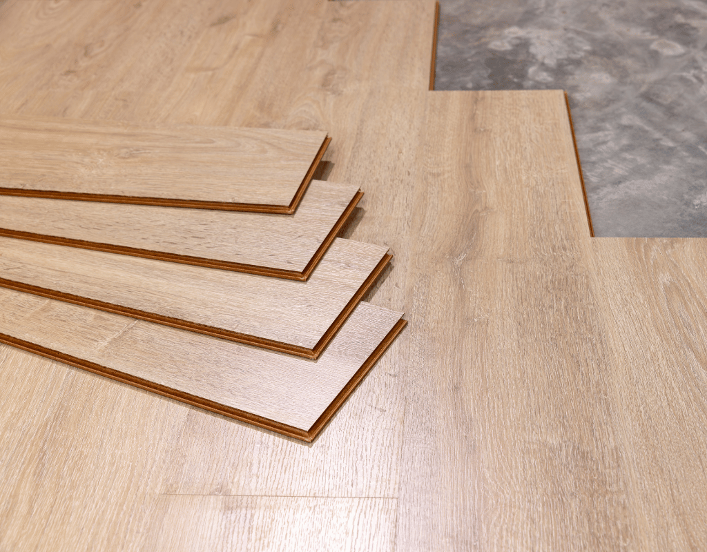 Fanned stack of light oak luxury vinyl planks lying on a finished floor next to a grey plank sample